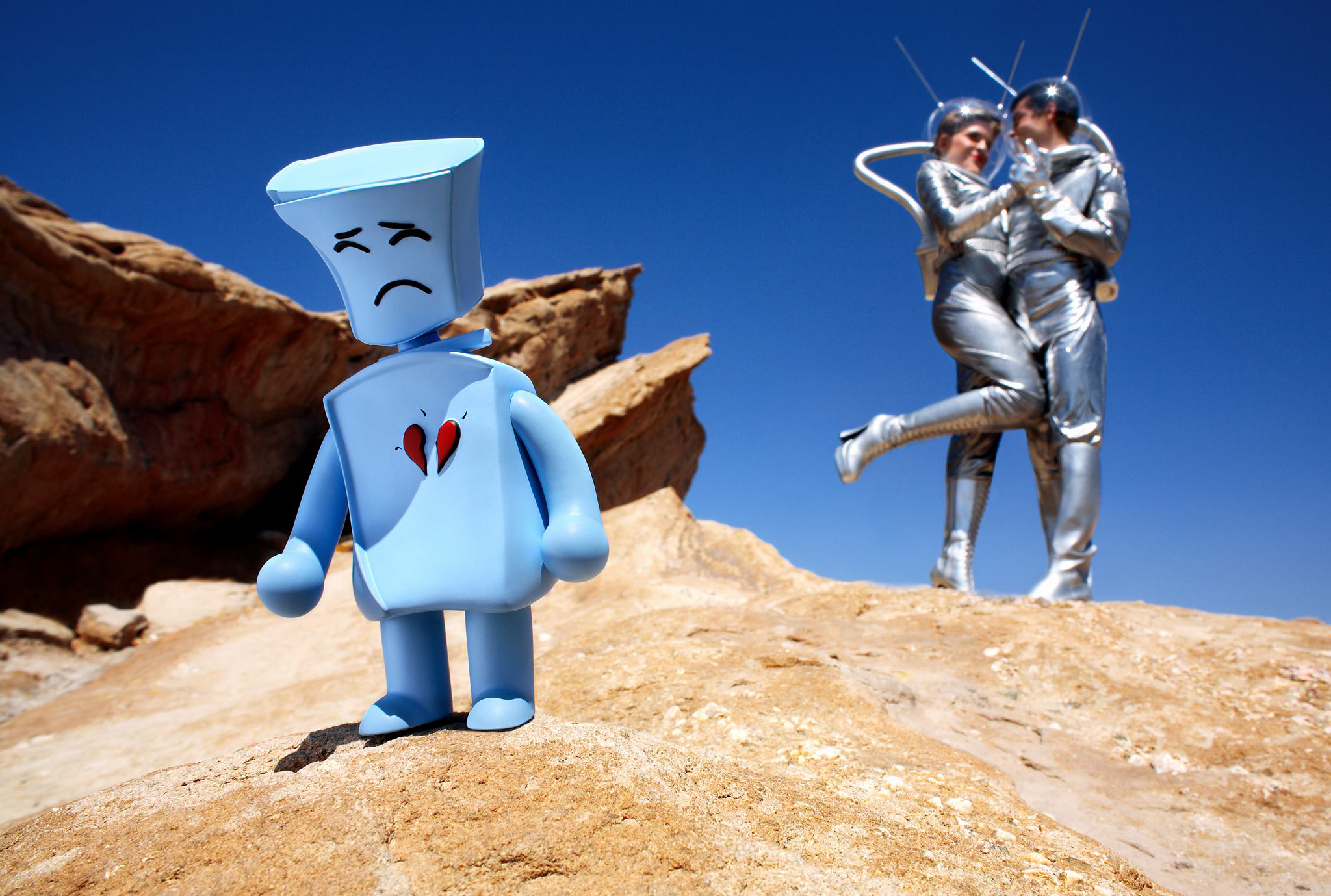 The blue Broken Heart Robot vinyl toy standing in a desert landscape